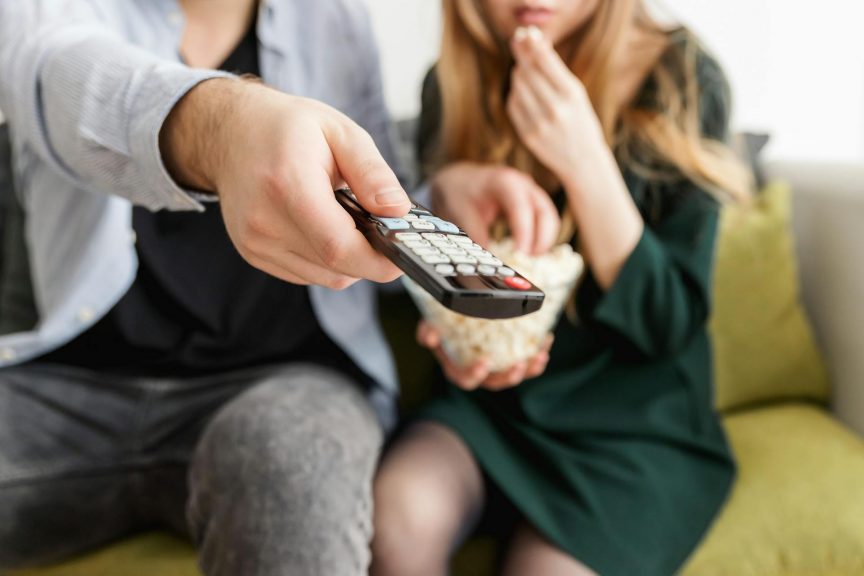 A couple watching TV on a sofa and using the remote control